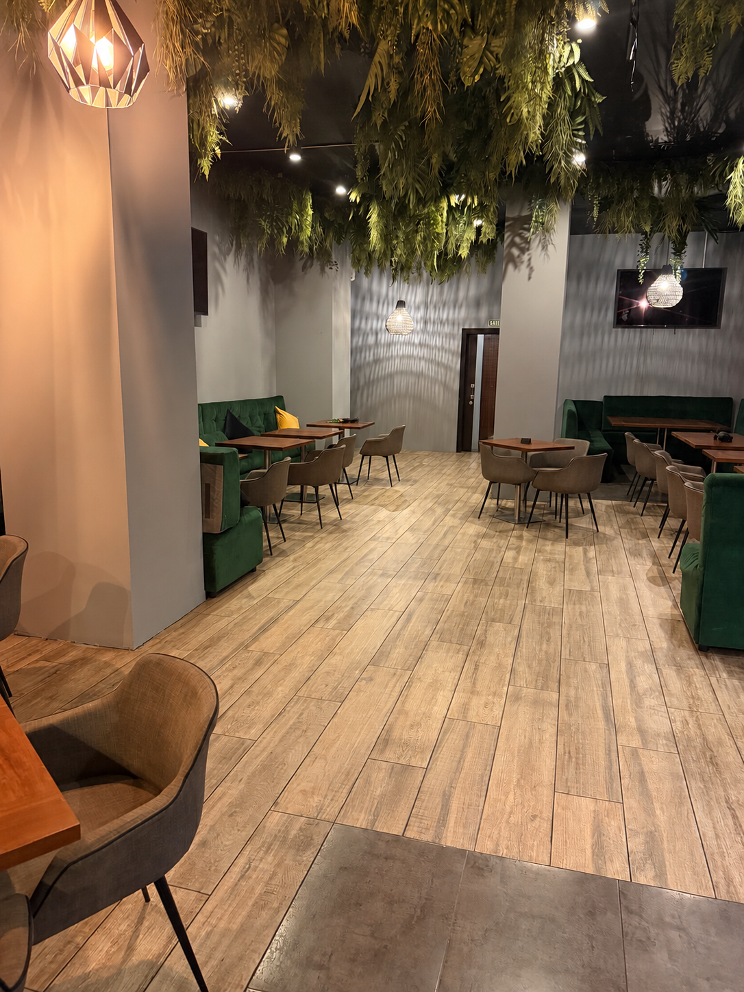 Vista general de La Trastienda, con mesas de madera, bancos verdes y vegetación en el techo